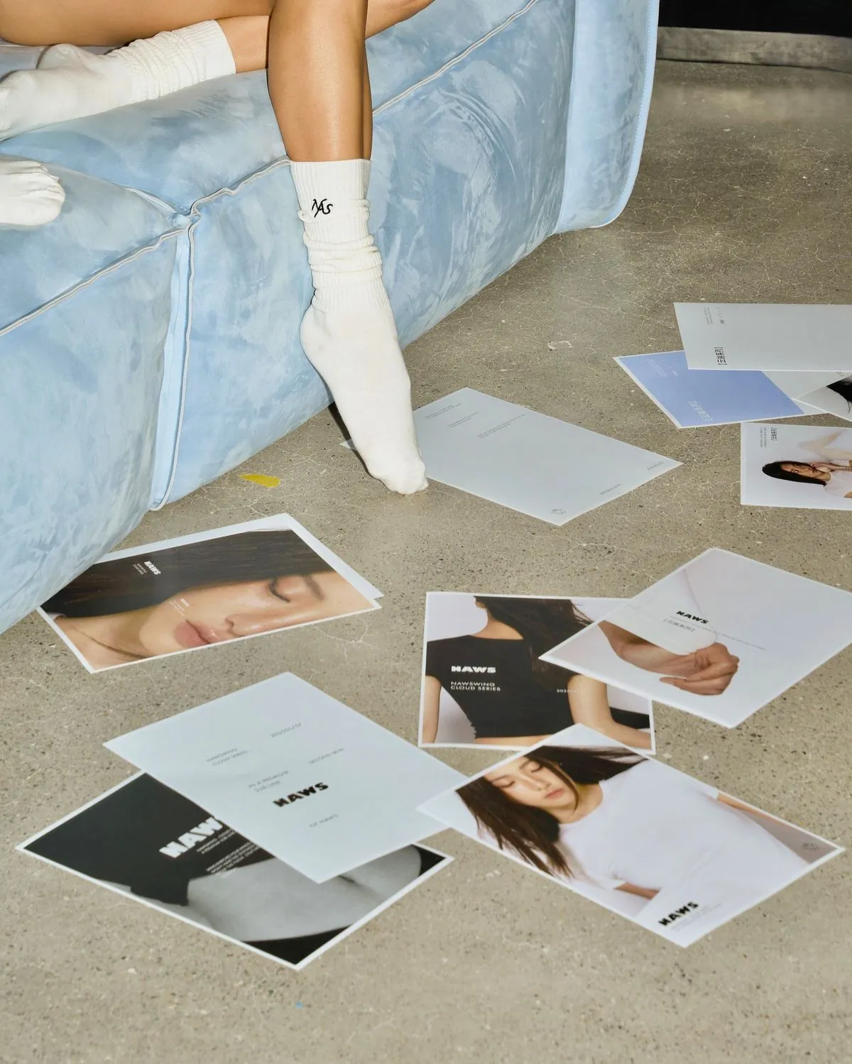 Campaign print layouts arranged around a pale blue sofa during a creative shoot